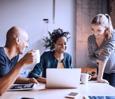 Zwei Frauen und ein Mann die zusammen arbeiten und auf einen Laptop schauen